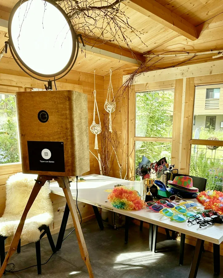 Fotobox Pro in einem Gartenhaus aus Holz, daneben ein langer Tisch mit Requisiten