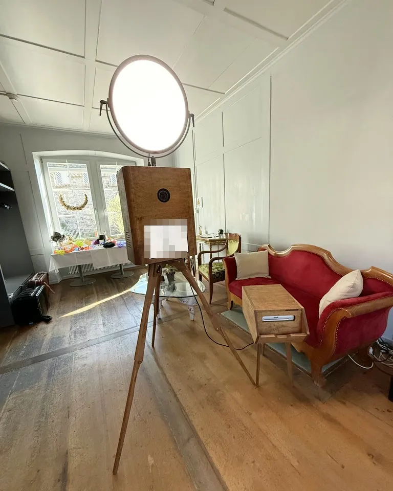 Fotobox Pro mit Druckerständer in einem hellen Raum neben einem roten Sofa